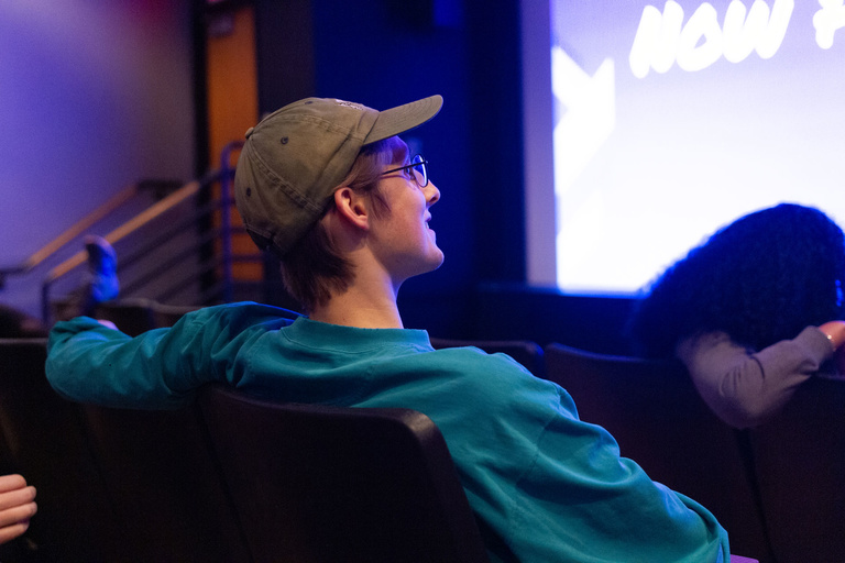 Person sitting on a movie theater seat in front of a film screen