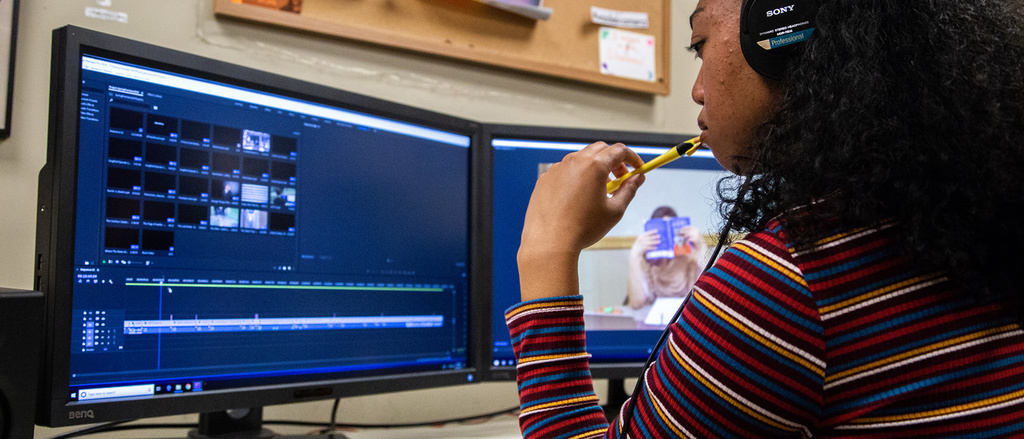 A person with headphones on looking at a computer screen with video editing software running on it